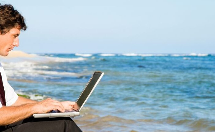 A man with remote work capabilities working in business attire on the beach.