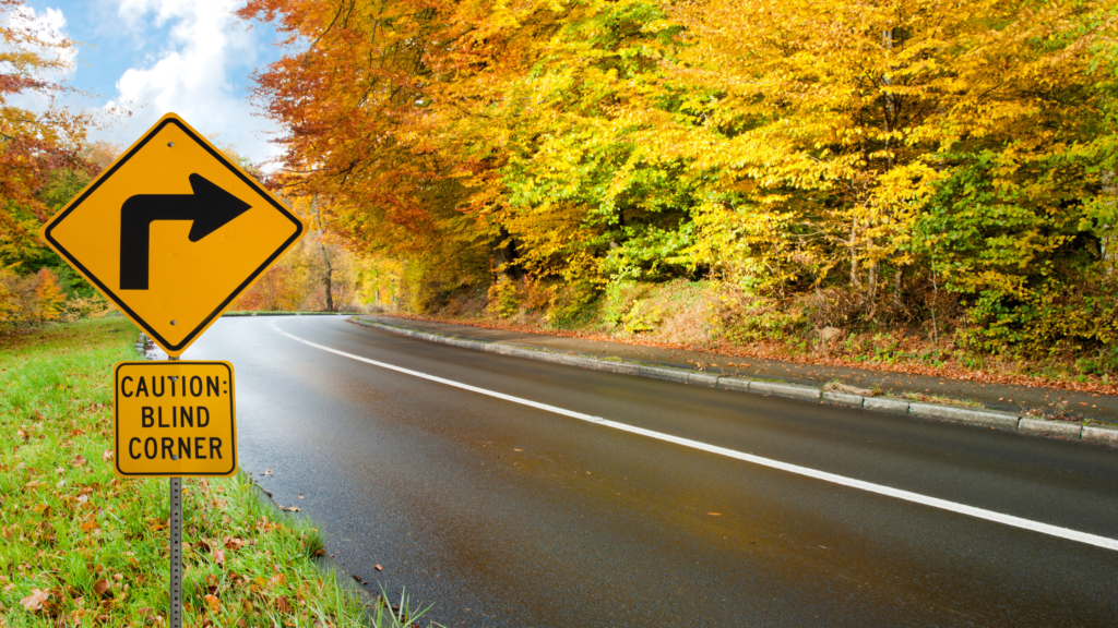 Winding forest road with blind corner sign, symbolizing hidden risks in your IT strategy.